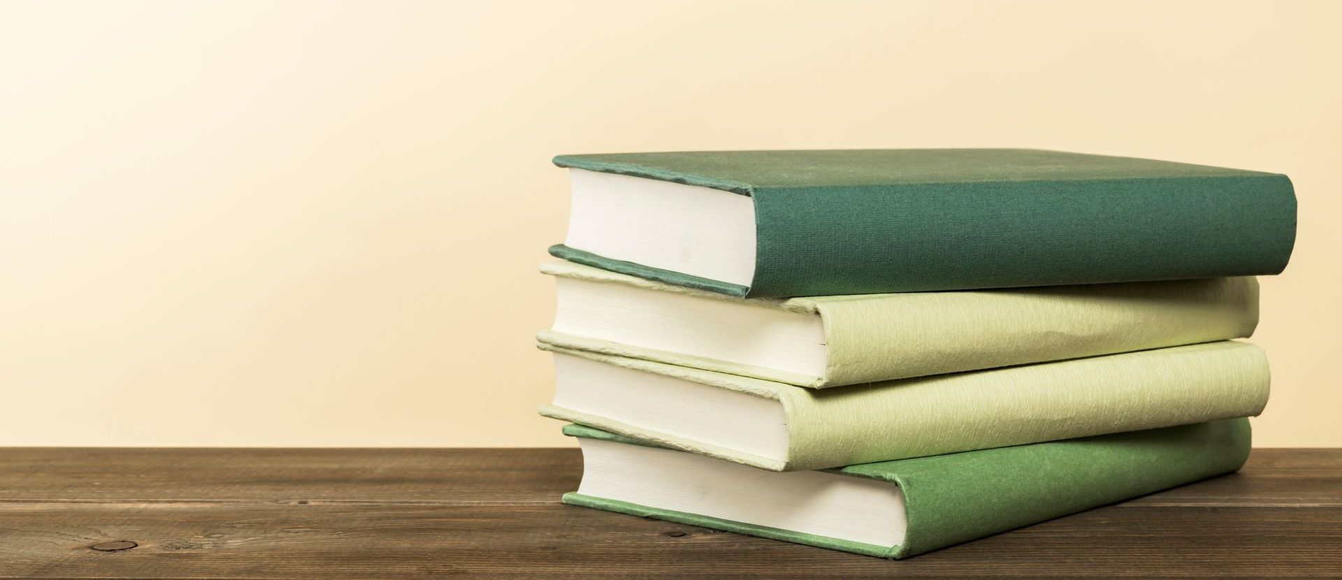 Tre libri verdi sono impilati uno sopra l'altro su un tavolo di legno.