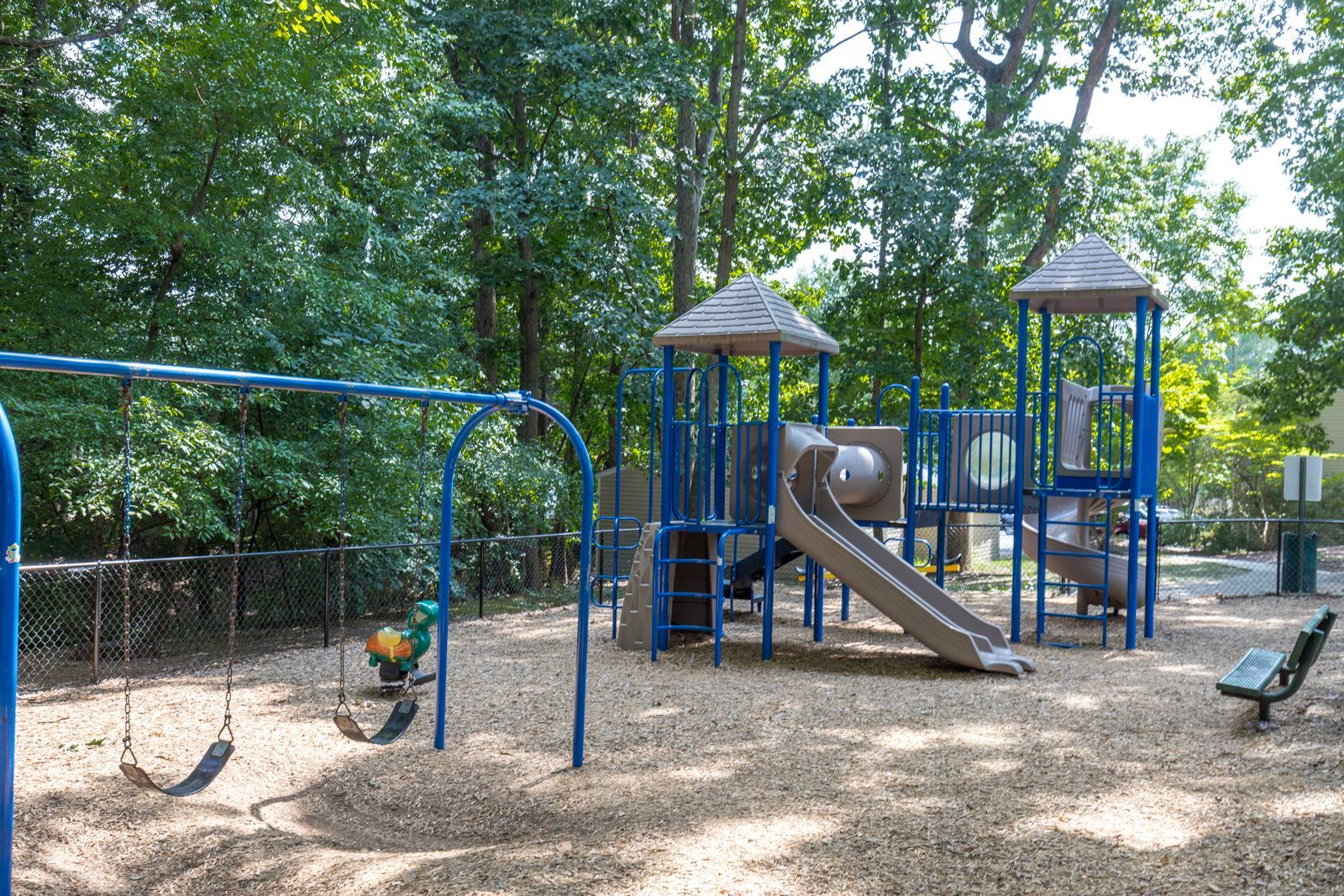 A playground with a slide, swings, and trees in the background.