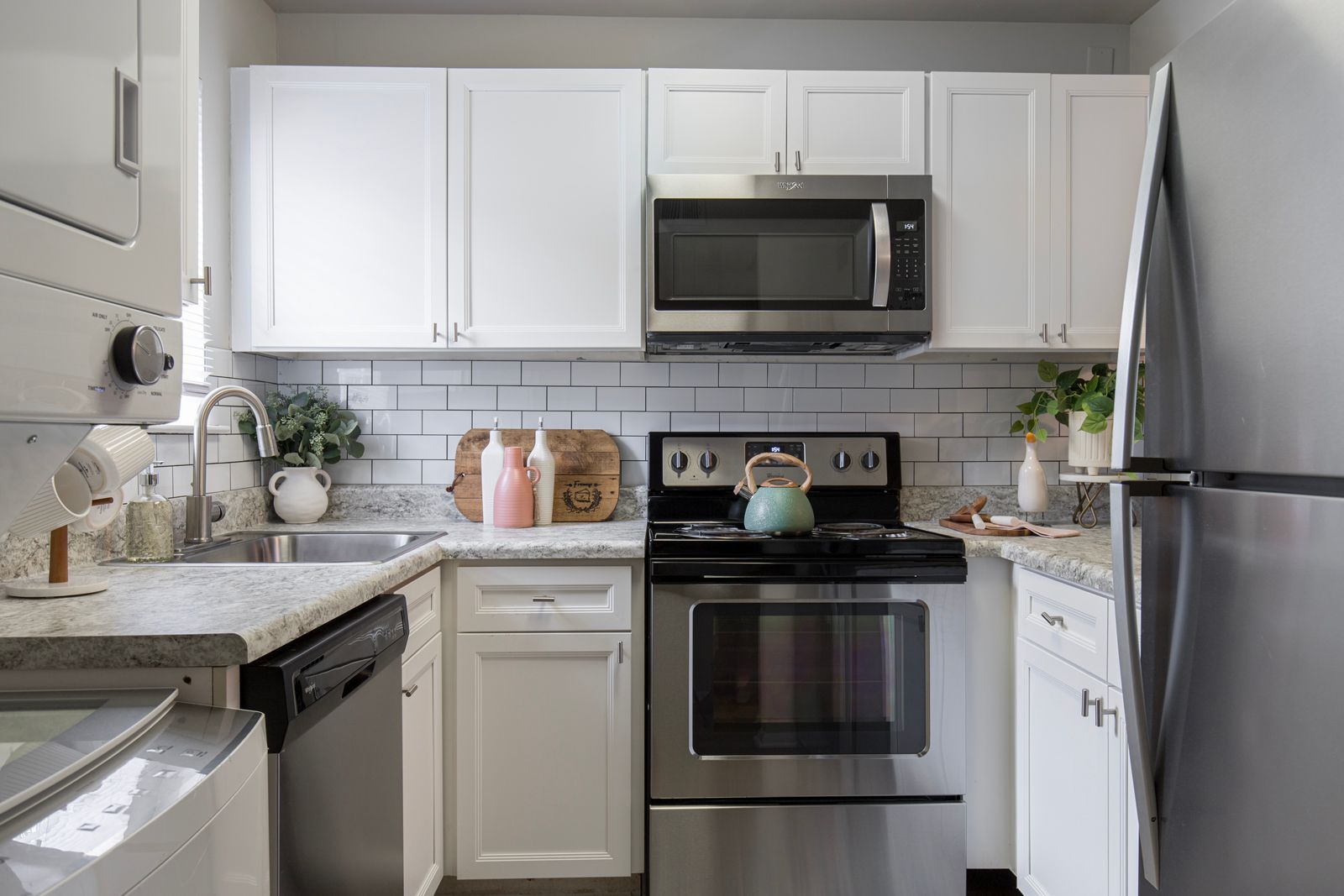 A kitchen with white cabinets, stainless steel appliances, a sink, and a refrigerator.