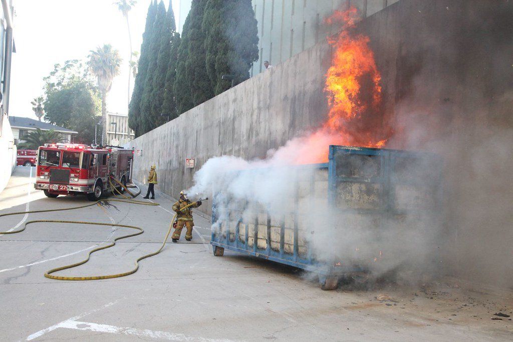 dumpster on fire with firefighter responders