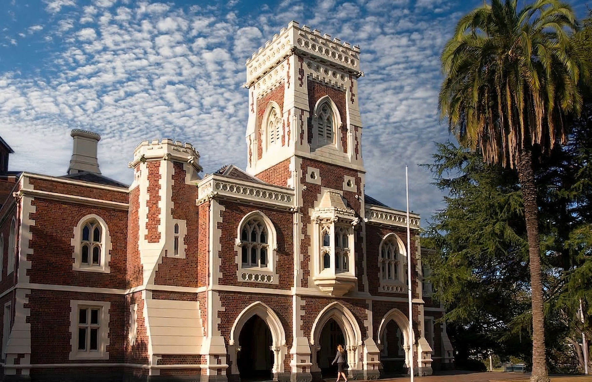 A person in a suit points toward a colleague across a wooden desk in an office with a computer and wall art.