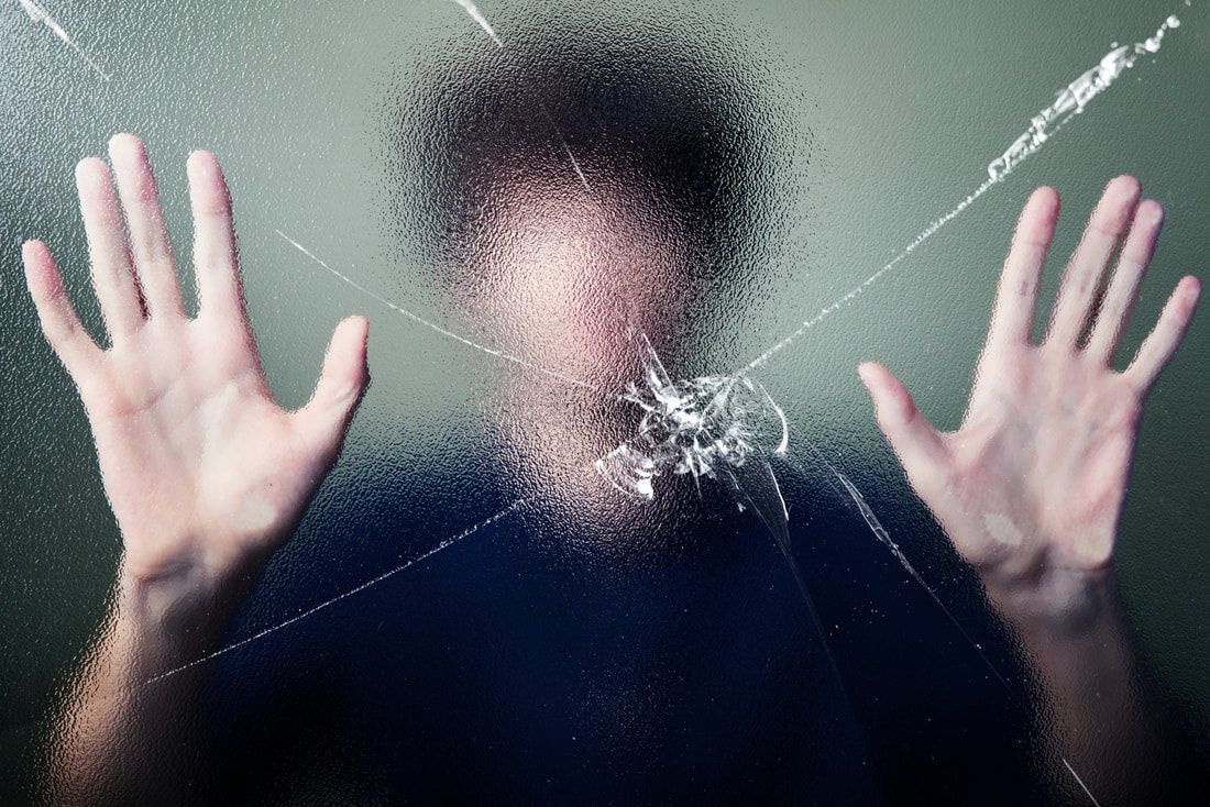 A person's hands are pressed against a pane of glass that is shattered in front of their face.