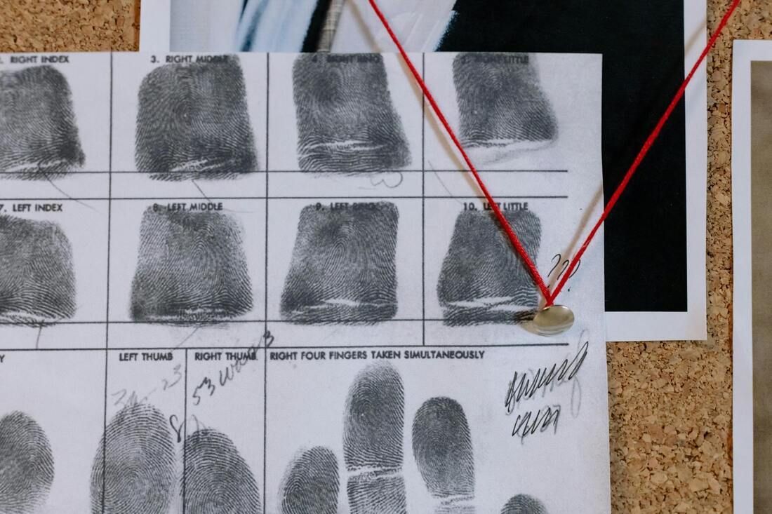 A fingerprint identification chart pinned to a corkboard, marked with a red string connected to a pushpin.