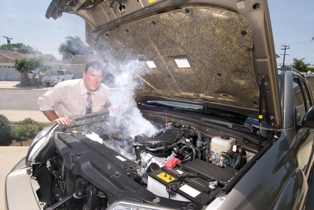 A man is looking under the hood of a broken down car