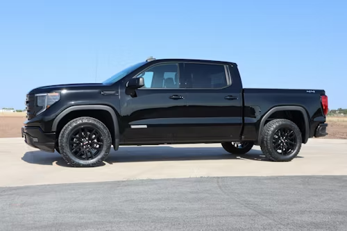 A black GMC Sierra crew cab pickup truck parked on a concrete surface against a clear blue sky.