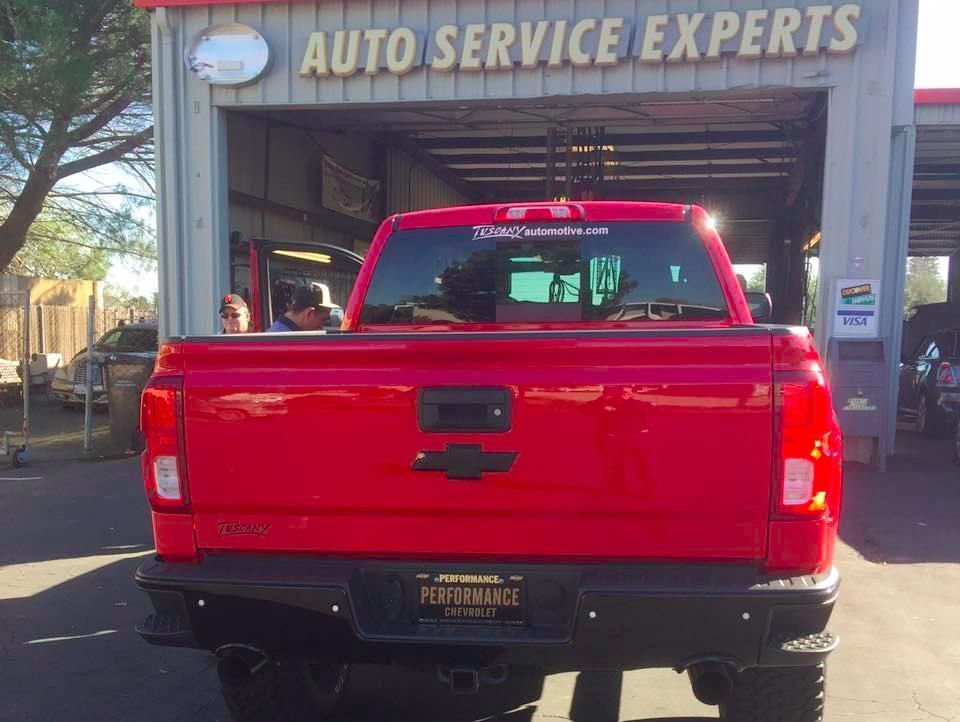 A red truck is parked in front of a building that says auto service experts