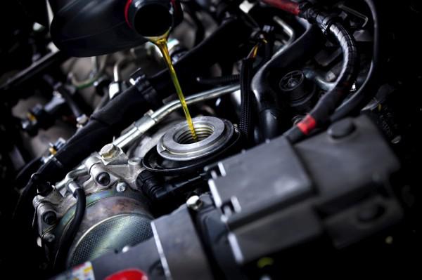 A close up of a person pouring oil into a car engine.