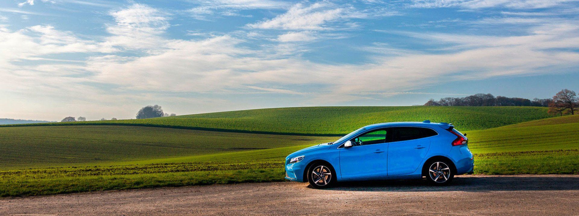 A blue car is parked on the side of a road next to a field.