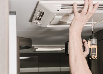 A person is fixing a ceiling fan with a drill.