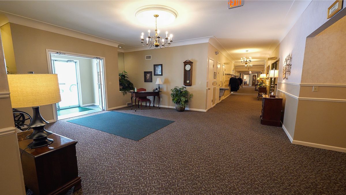 Long hallway with brown carpet, neutral walls, and ornate ceiling fixtures. Entry doorway on the left.
