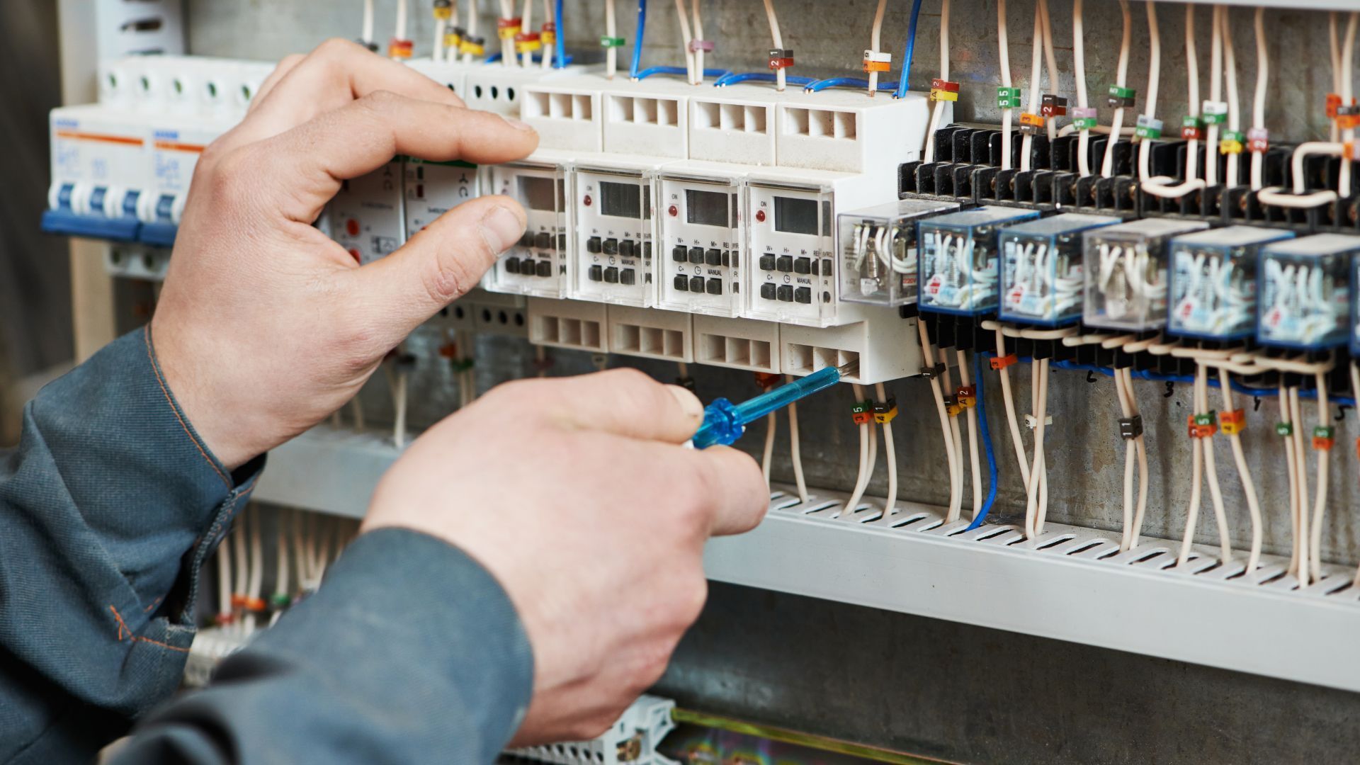 A man is working on an electrical panel with a screwdriver.