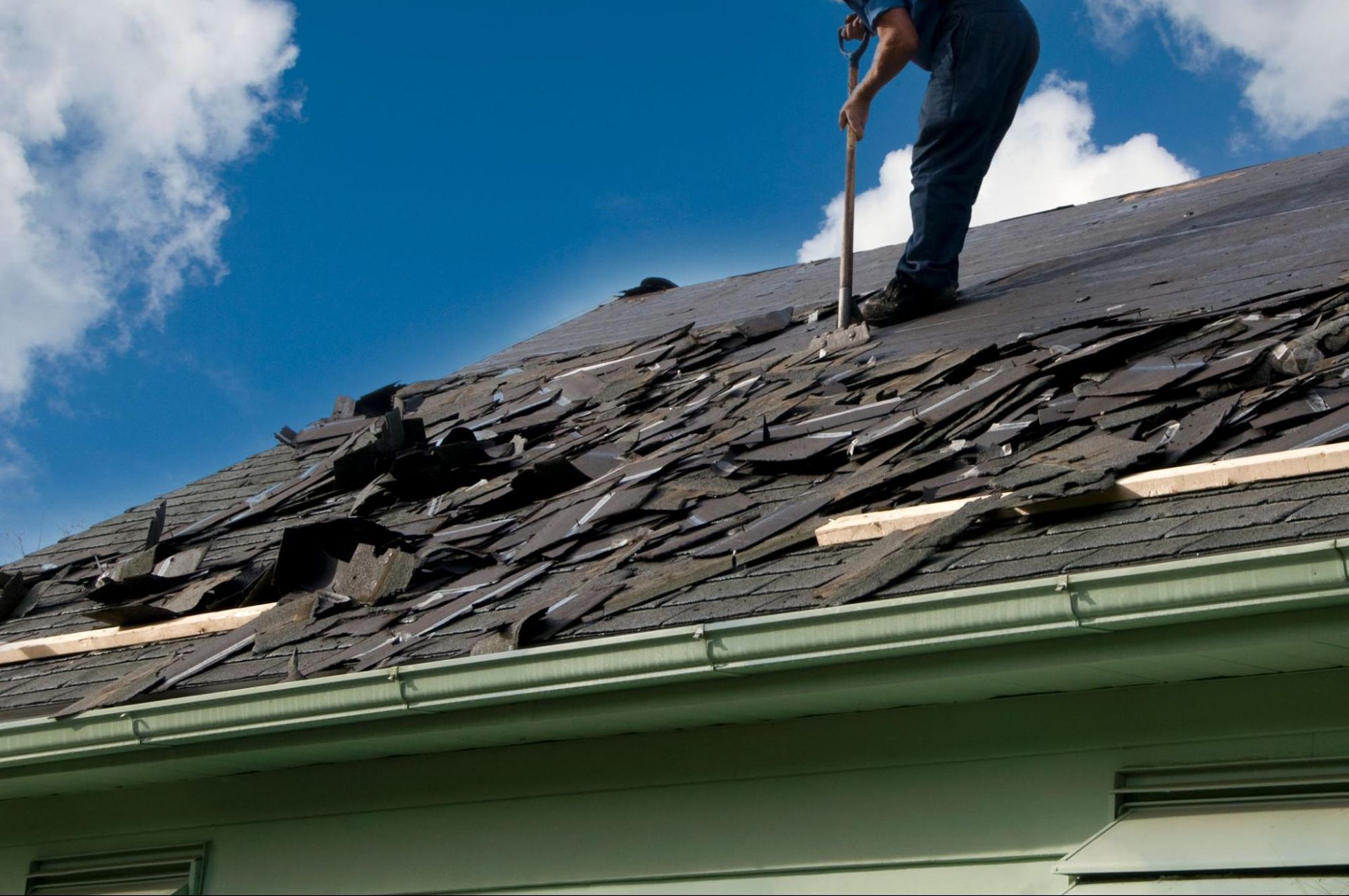 A man is standing on top of a roof with a hammer.