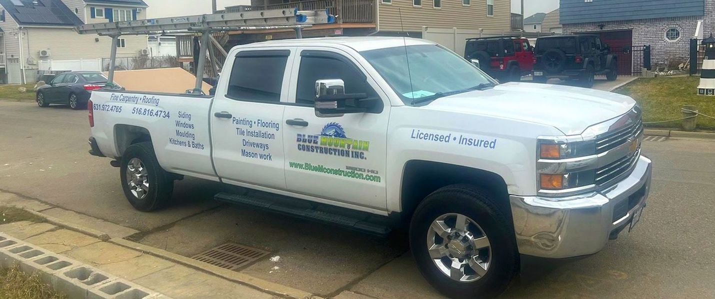 A man is standing on a ladder in front of a house with a truck parked in front of it.