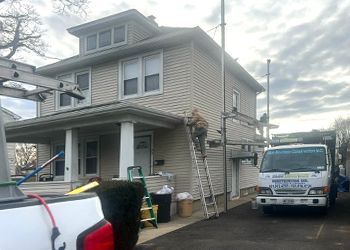 A man is standing on a ladder in front of a house with a truck parked in front of it.