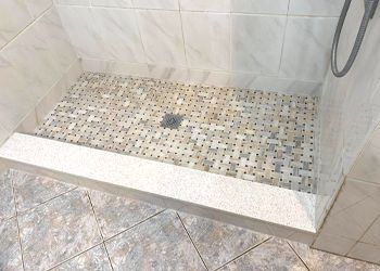 A walk in shower with a tiled floor and a glass door.