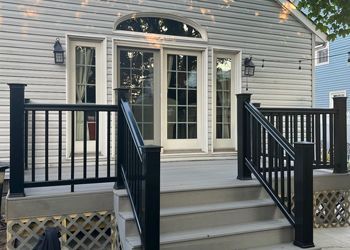 A white house with a black deck and stairs leading to it.