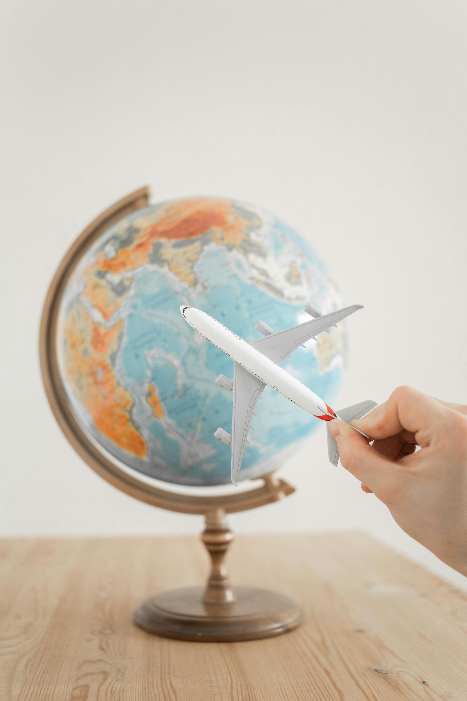 Hand holding a toy airplane over a globe, suggesting travel.