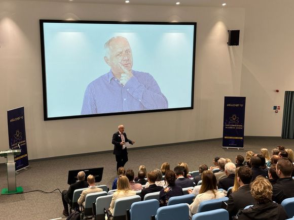 Peter Barker is giving a presentation in front of a large screen in a lecture hall.