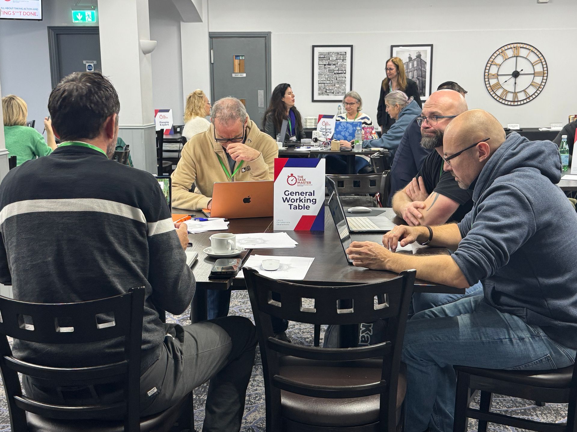 People seated at tables in a conference room, some using laptops and talking.
