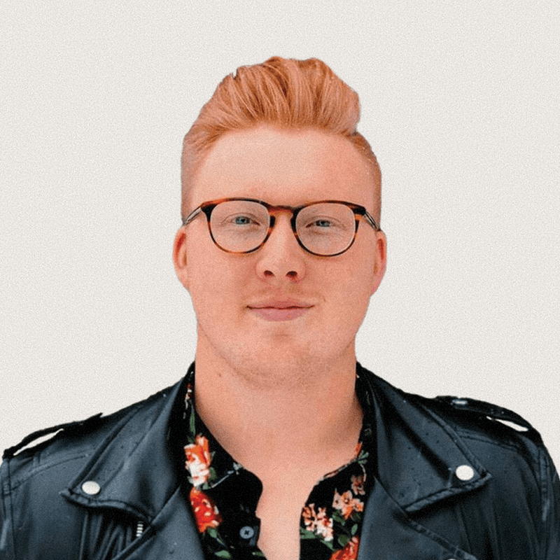 A man with red hair wearing glasses and a leather jacket