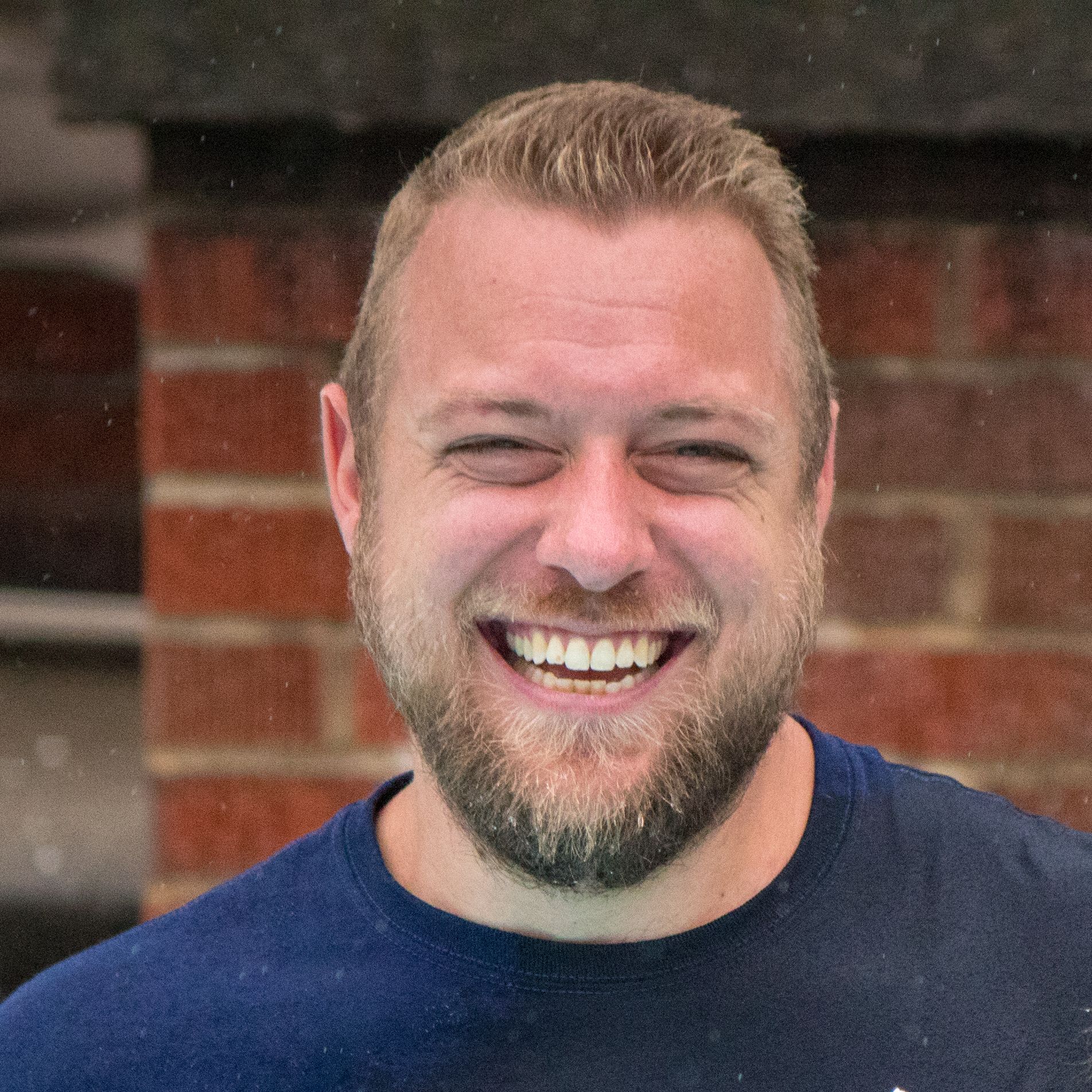 Woman with curly red hair smiles, wearing black, in front of a building.