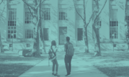Two students talking on a path in front of a college building, teal-toned filter.