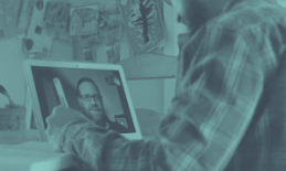Man on video call, pointing at laptop screen. Teal-toned.