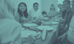 Family smiling around a table with food, inside a home.