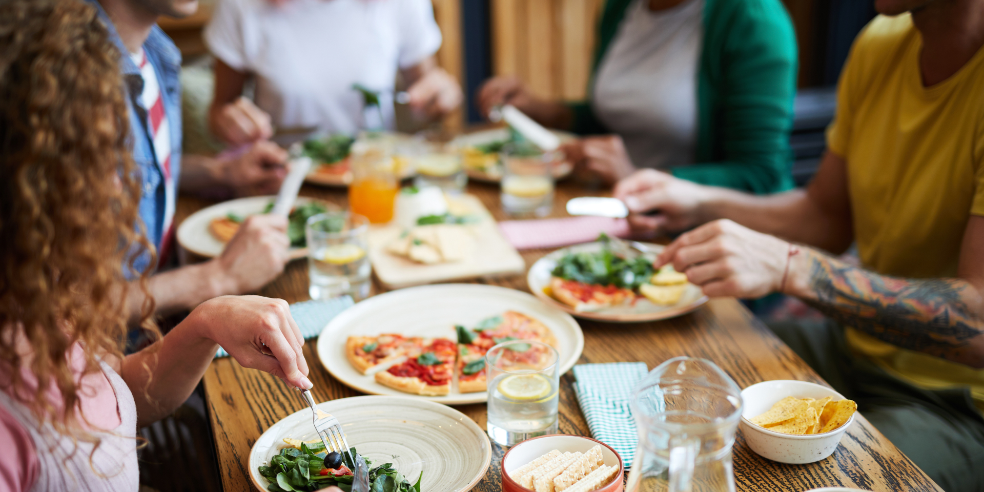 People gathered at a buffet table with food, balloons, and a large window in the background.