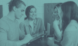 Four people smiling and looking at a tablet together in an office setting.