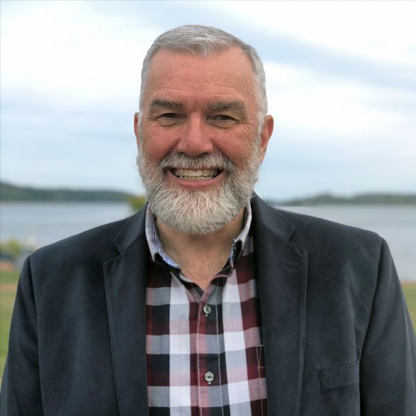 Man smiling with beard and blazer in front of body of water