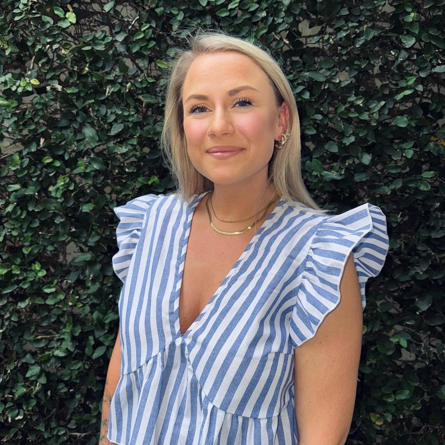 Woman with blonde hair and blue and white striped shirt, smiling, standing outside.