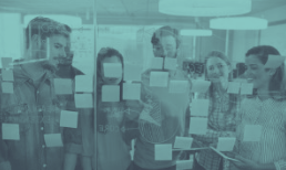 Group of people brainstorming, standing near a glass wall covered in sticky notes, indoors.