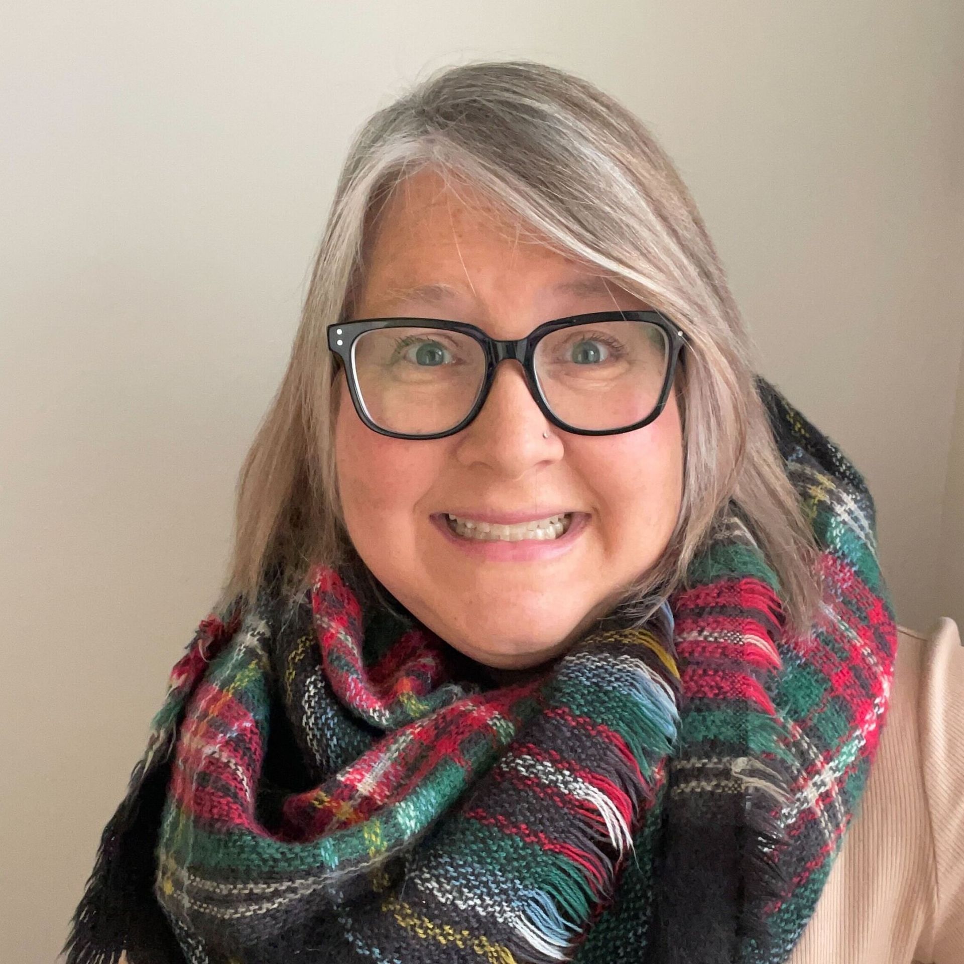 Woman with glasses and a plaid scarf smiles.