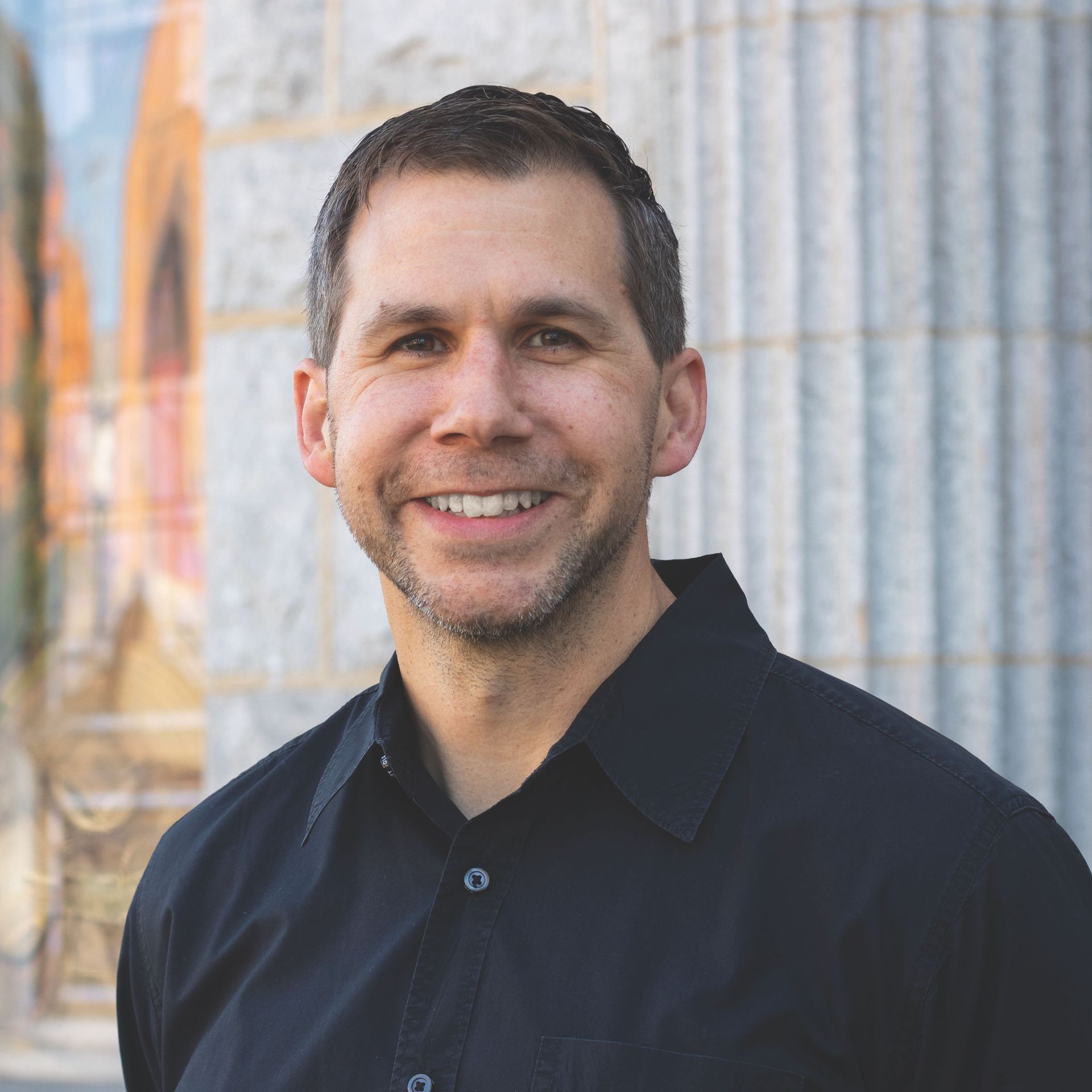 man smiles at camera in front of building