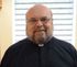 A man with glasses, a beard, and clerical collar smiles at the camera.