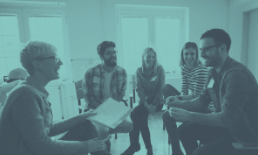 Group therapy session: People sitting in a circle, laughing, sharing papers.