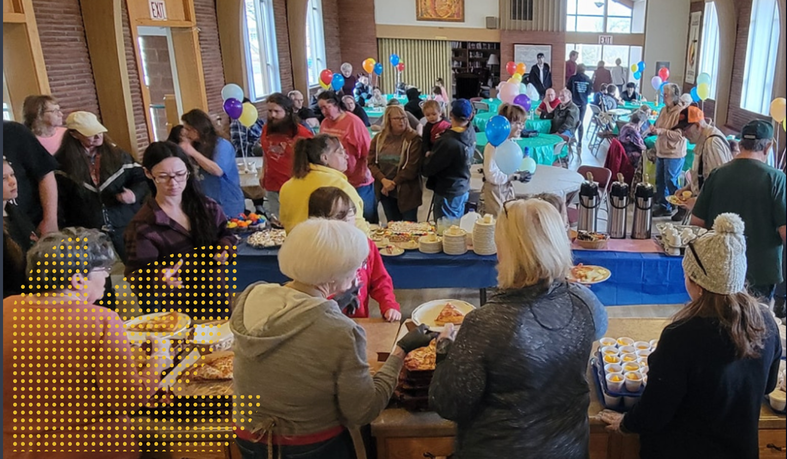 People gathered at a buffet table, balloons in background. Indoor event, various ages, eating and socializing.