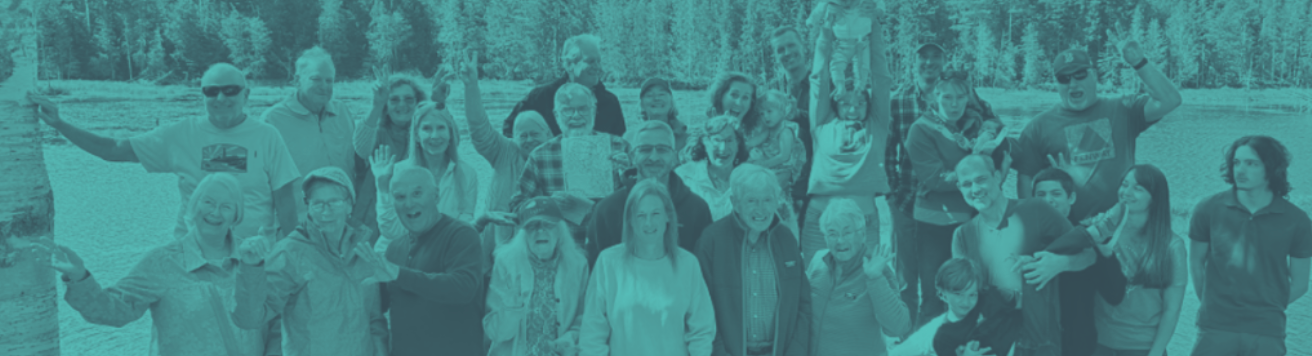 Group of people outdoors, with smiles and arms raised, in front of a background of trees.