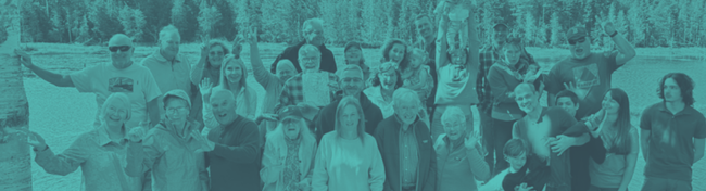 Group of people outdoors, with smiles and arms raised, in front of a background of trees.