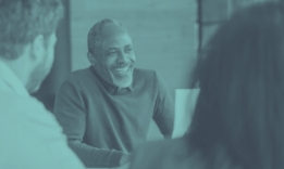 Man smiles while talking with others at a table.