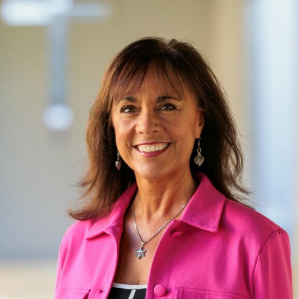 Man with a beard smiling, wearing a hat and plaid shirt, standing in a city street.