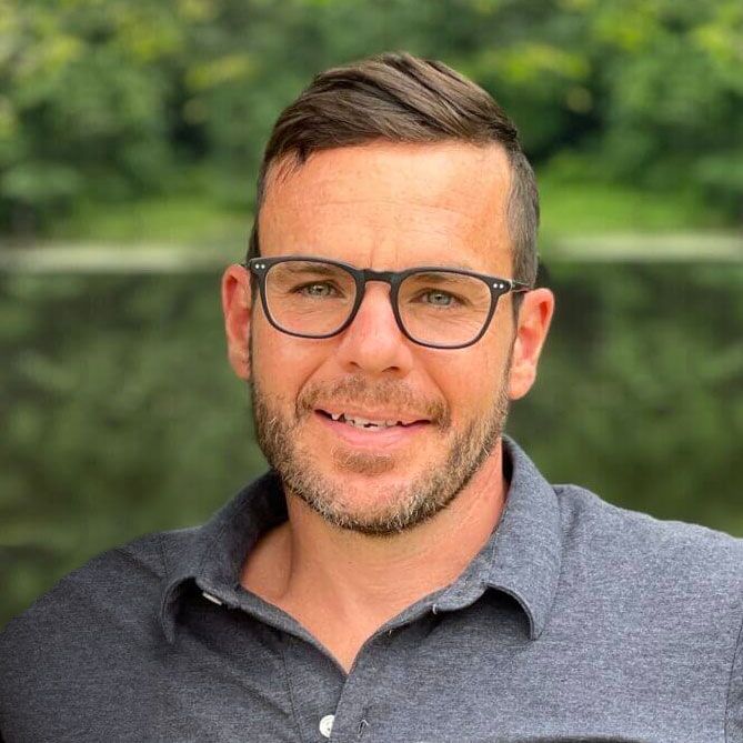 Man with red hair and beard smiles at the camera against a brick wall background.