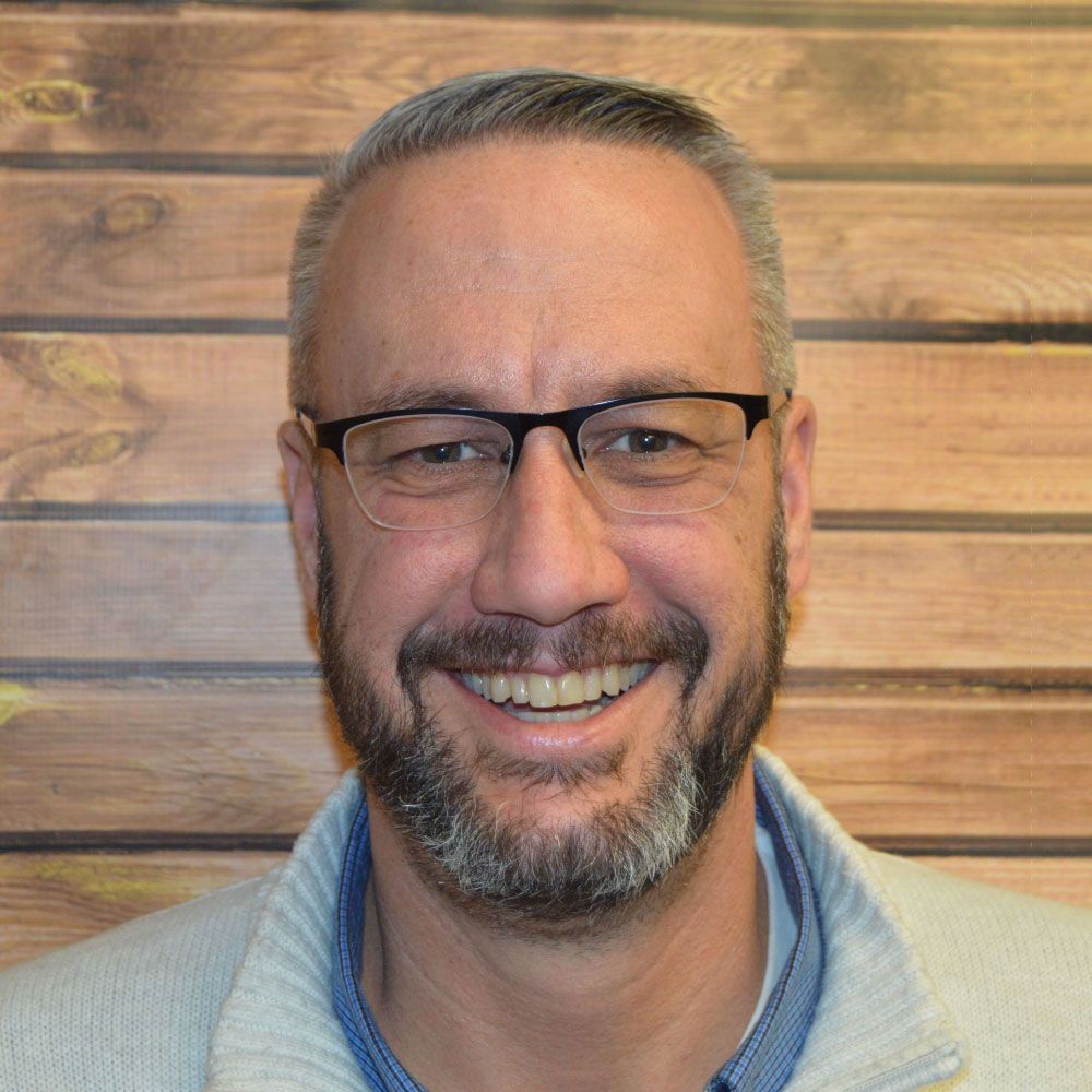 man with glasses smiling at camera in front of wood paneling