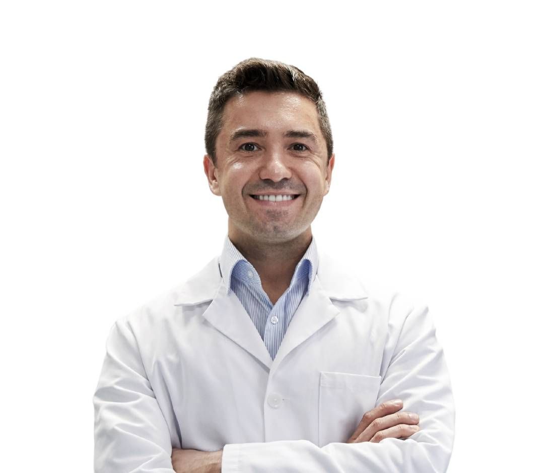 Un uomo in camice bianco sorride con le braccia incrociate.