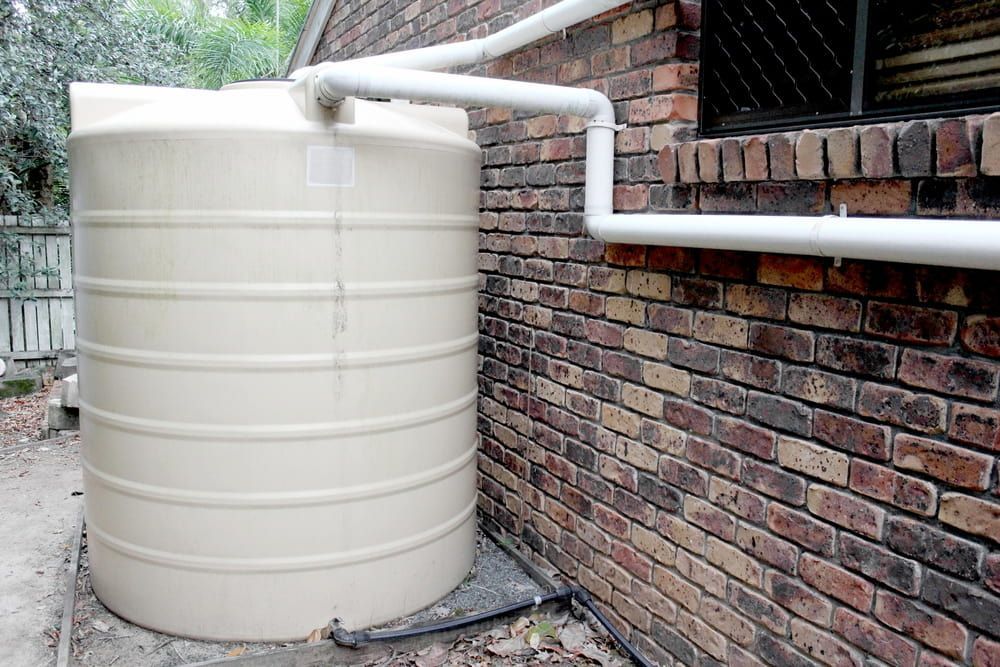 Beige Water Tank With Pipe by Brick Wall — Primed Plumbing & Gasfitting in Eglinton, NSW