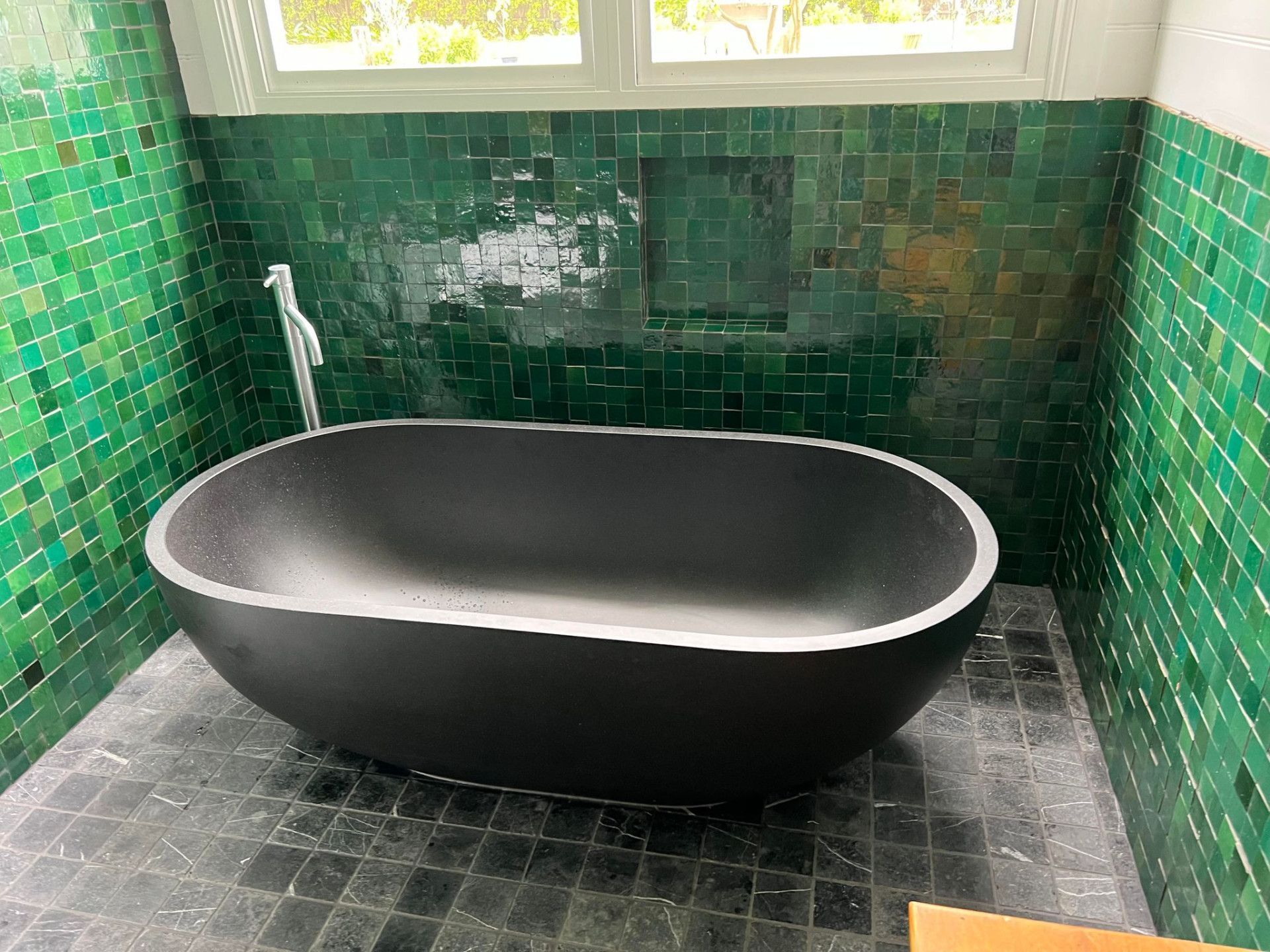 A black bath tub with bright green tiles surrounding wall— Primed Plumbing & Gasfitting in Eglinton, NSW