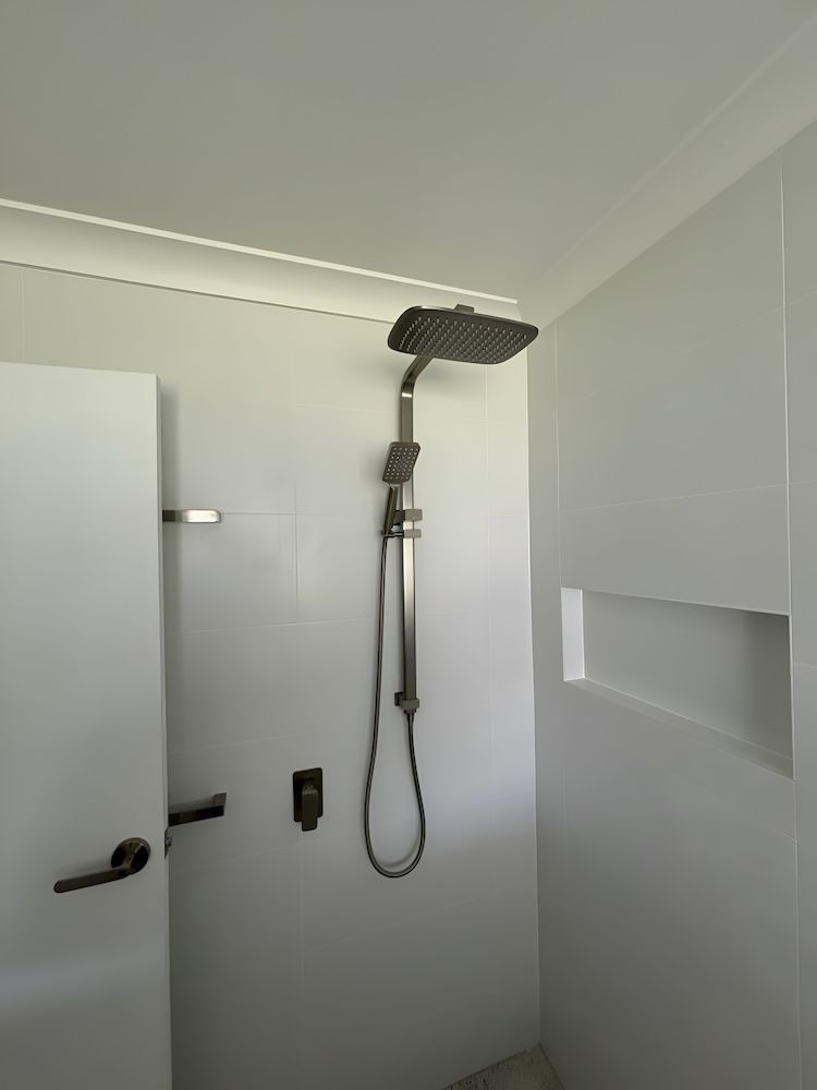 A White Bathroom With a Shower Head, Faucet, and Alcove — Primed Plumbing & Gasfitting in Eglinton, NSW