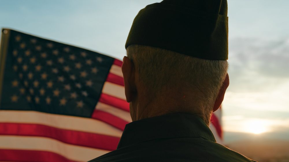 A man in a military uniform is standing in front of an american flag.