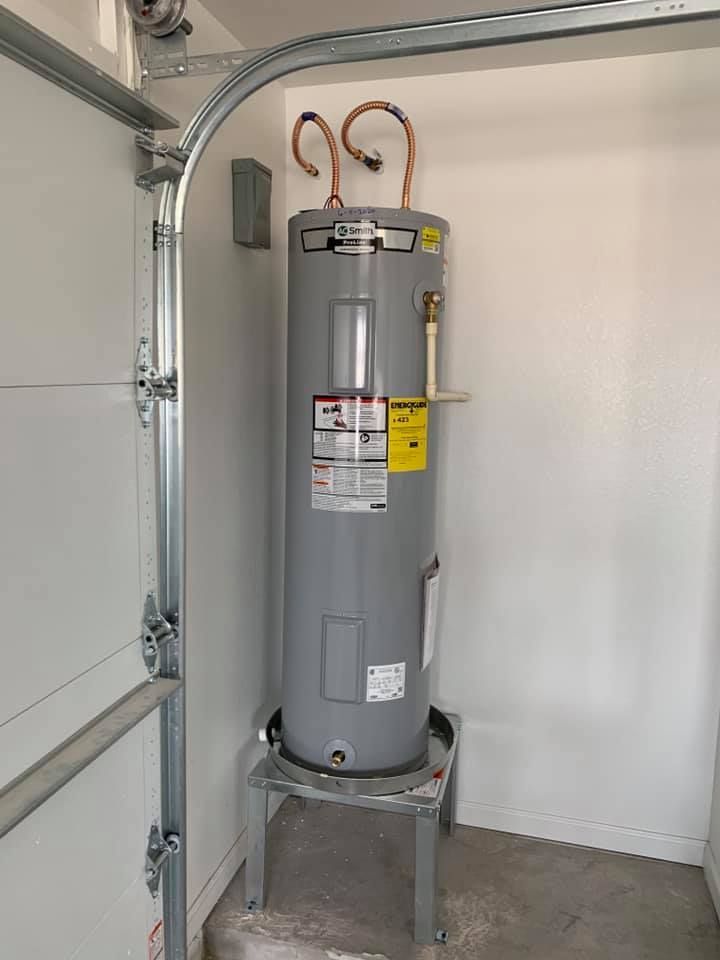 A water heater is sitting in a garage next to a garage door.